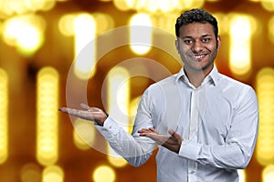 Handsome businessman looking at camera while presenting something on golden bokeh background.