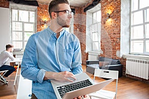 Handsome businessman is looking out the window and smiling while standing in office.