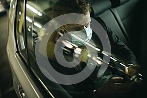 Handsome businessman in medical mask using mobile phone in car, concept of coronavirus quarantine