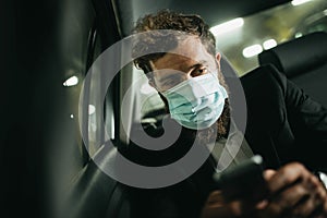 Handsome businessman in medical mask using mobile phone in car, concept of coronavirus quarantine