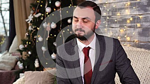 Handsome businessman nods in dissenting near christmas tree in cozy room with holidays decorations