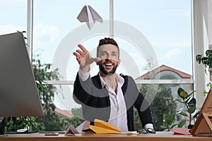 Handsome businessman playing with paper plane at desk in office