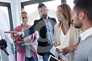 Handsome businessman pointing at white blackboard and explain a project to her colleagues on coworking place