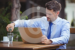 Handsome businessman pouring drink in glass while using laptop