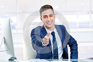 Handsome businessman reaching out hand at desk.