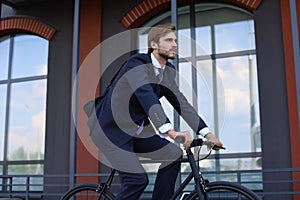 Handsome businessman riding bicycle to work on urban street in morning.