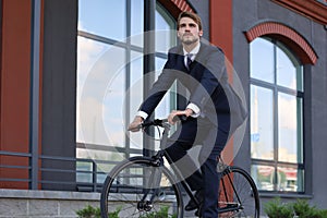 Handsome businessman riding bicycle to work on urban street in morning