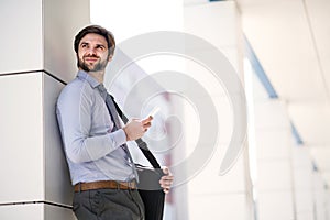 Handsome businessman scrolling on smartphone standing in front office building going to work. Manager smiling, outdoor