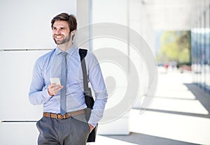 Handsome businessman scrolling on smartphone while walking on city street, going to office. Manager smiling, outdoor in