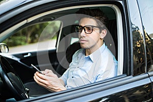 Handsome businessman sending a text message in his car