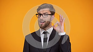 Handsome businessman showing ok sign and winking, isolated on orange background