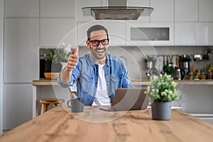 Handsome businessman showing thumbs up sign while working over laptop on desk in home office