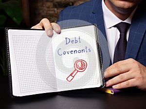 A handsome businessman showing a white notepad with sign Debt Covenants . Close-up shot. Soft focus