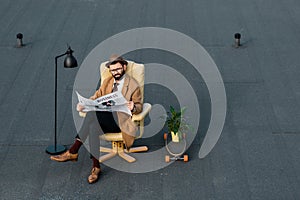 handsome businessman sitting in armchair and reading newspaper
