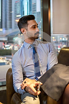 Handsome businessman sitting in a cafe, holding mobile phone in hand and looking away