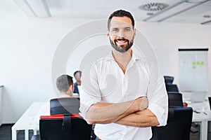 Handsome businessman standing at office looking at camera