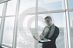 Handsome businessman in suit and eyeglasses work with laptop in hands in office