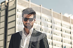 Handsome businessman with sunglasses, outdoor in the city. Charming and modern style, with shirt and suite. Cool hairstyle. Behind