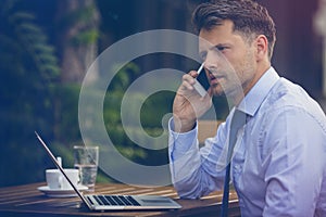 Handsome businessman talking on mobile phone while using laptop