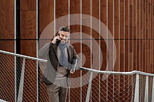 Handsome businessman talking on smart phone and smiling on a terrace outside office, working.