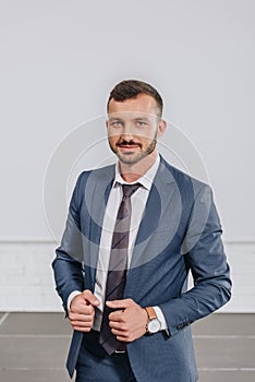 handsome businessman touching jacket and looking at camera