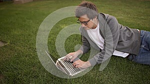 Handsome businessman typing on his laptop lying on a lawn, top view