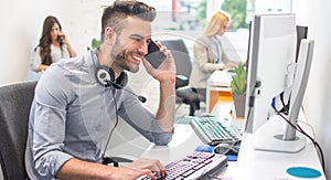 Handsome businessman using a computer, talking on the mobile phone and smiling while working in office.