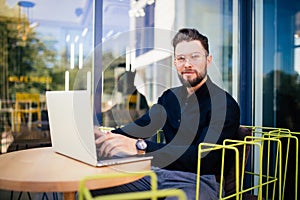 Handsome businessman using modern laptop outdoors, successful manager working in cafe during break and searching information in in