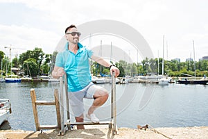 Handsome businessman on vacation with yachts on dock background. Sport Man in sunglasses laddering up on boat