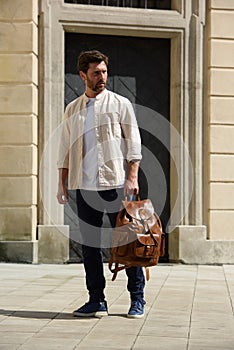 Handsome businessman walking on the street, with luxury leather brown backpack. Fashionable style.