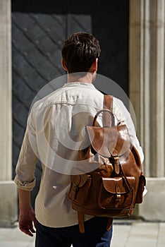 Handsome businessman walking on the street, with luxury leather brown backpack. Fashionable style.