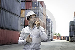 Handsome businessman wearing safety helmet,  using walkie talkie and holdigital table  during inspection at logistic shipping