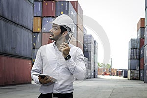 Handsome businessman wearing safety helmet,  using walkie talkie and holdigital table  during inspection at logistic shipping