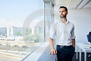 handsome businessman at work standing at office looking out window