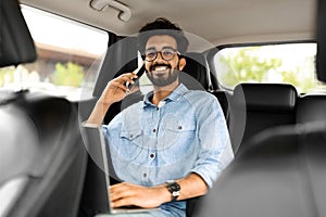 Handsome businessman working on laptop, talking on phone in car