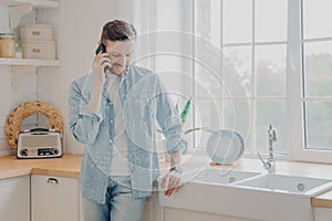 Handsome busy bearded businessman in casual comfy clothes standing in kitchen with mobile phone