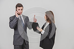 Handsome busy businessman is talking on the phone, pointing his finger up for his secretary to wait. Secretery standing photo