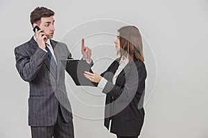 Handsome busy businessman is talking on the phone, pointing his finger up for his secretary to wait. Secretery standing photo