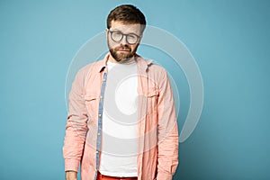 Handsome, calm, bearded man with glasses narrowed eyes and looks at the camera suspiciously.