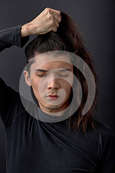 Handsome calm man holding straight long hair in hands with eyes closed, isolated on black