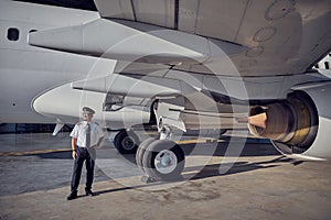 Handsome captain in hat looking into the distance in front of civil aircraft