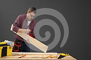 Handsome carpenter working with timber at table on background. Space for text