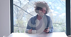 Young man drinking coffee and using a mobile phone at home