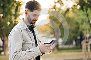 Handsome caucasian armenian young bearded man using phone stand on street at sunset. Mobile technology. Businessman cell