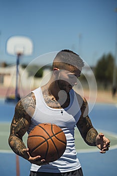 Handsome caucasian basketball player with cool tattoos standing on the court holding the ball