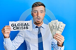 Handsome caucasian business man holding dollars on global crisis afraid and shocked with surprise and amazed expression, fear and