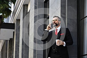 Handsome Caucasian business man using mobile phone and holding take away coffee cup outside apartment in the morning