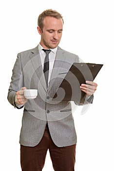 Handsome Caucasian businessman reading clipboard while drinking