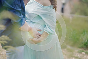 Handsome Caucasian couple holding hands with focus on the pregnant woman`s beautiful round tummy