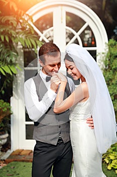 Handsome caucasian groom is holding and kissing asian bride hand with love and smiling face during wedding or pre wedding photo